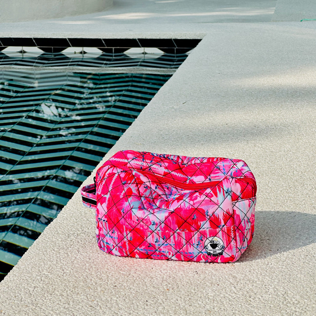 Pink and white patterned toiletry bag on a concrete surface near a pool.